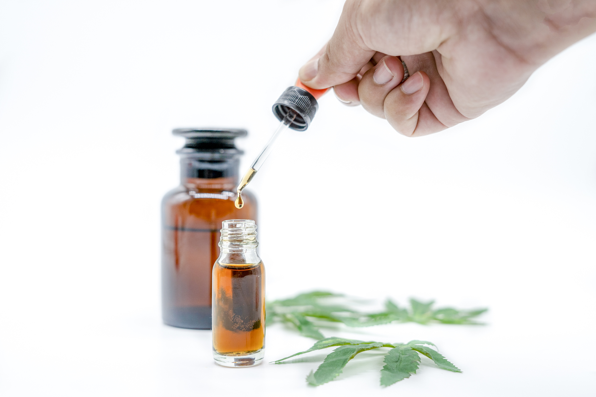 A person's hand holding a dropper over a small bottle of CBD oil
