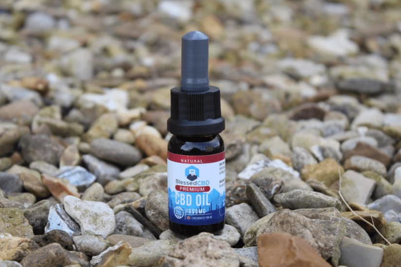 A bottle of Blessed CBD Premium CBD oil standing on a bed of small rocks